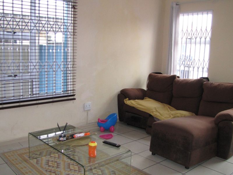 A living room featuring tiled flooring, security gates on windows, and venetian blinds. The space requires minor cosmetic updates to the wall finishes.