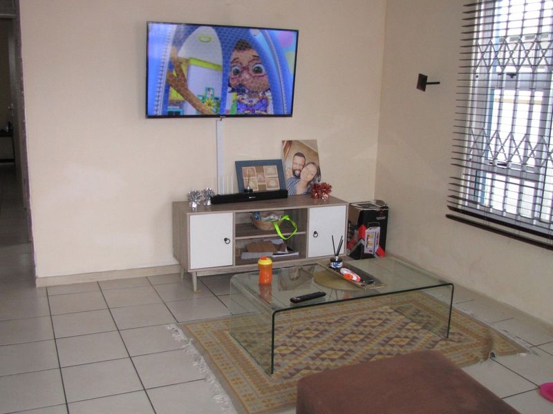A functional living room featuring tiled flooring, a window with security bars, and venetian blinds, providing a neutral base for interior updates.