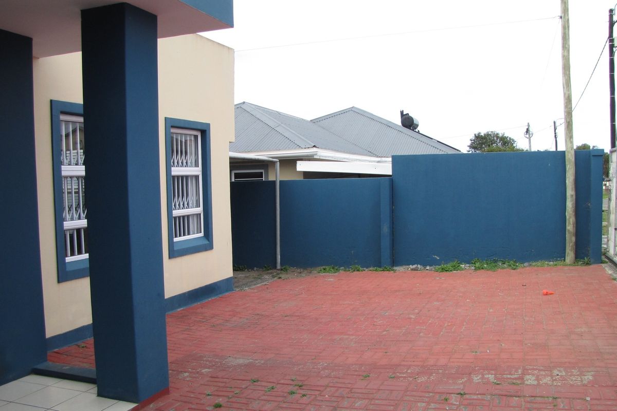 A rear exterior view featuring a paved courtyard area, boundary wall, and building facade with security-fitted windows.