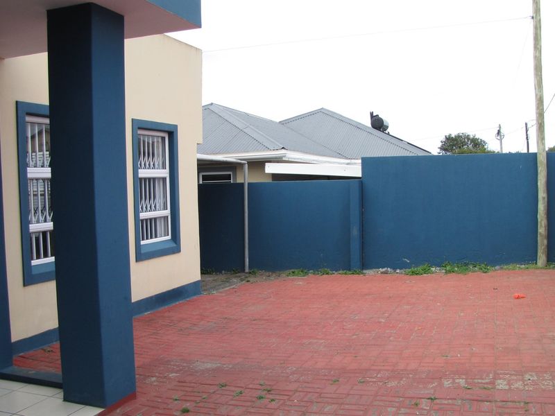 A rear exterior view featuring a paved courtyard area, boundary wall, and building facade with security-fitted windows.
