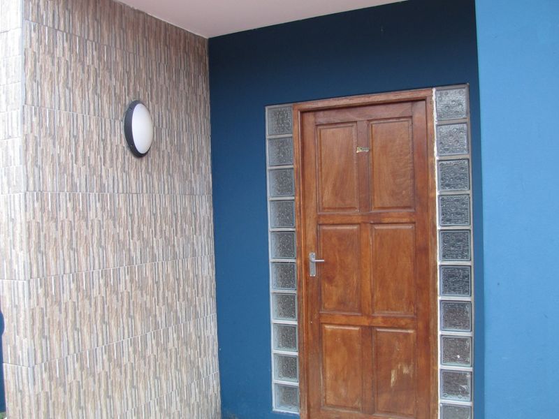 Entrance area featuring a timber front door flanked by glass block sidelights, complemented by textured wall tiling and a blue painted exterior finish.