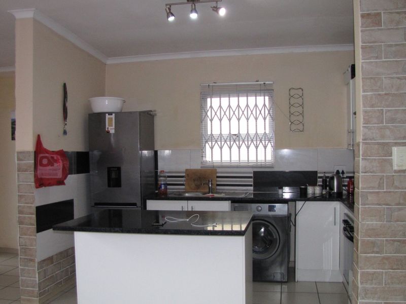 Functional kitchen featuring granite countertops, white cabinetry, tiled flooring, and a decorative brick-style feature wall with integrated lighting.