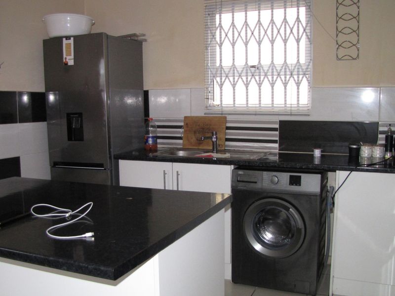 A functional kitchen featuring modern white cabinetry, dark granite countertops, a tiled backsplash, and a security gate on the window.
