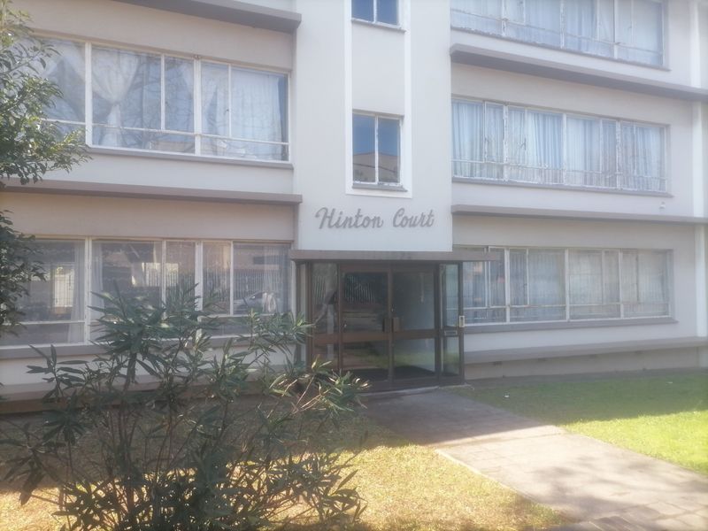 Front facade of Hinton Court apartment building featuring a glass entrance door, metal-framed windows, and a paved walkway.