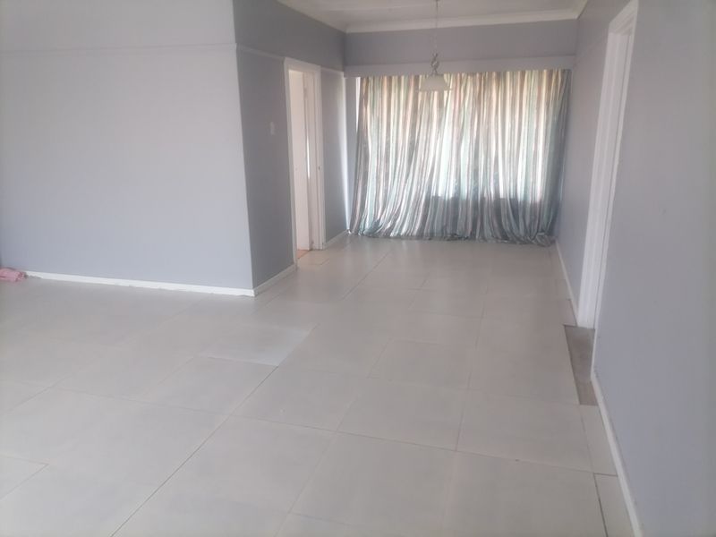 An empty, neutrally painted living area featuring tiled flooring and a ceiling pendant light, ready for personalization.