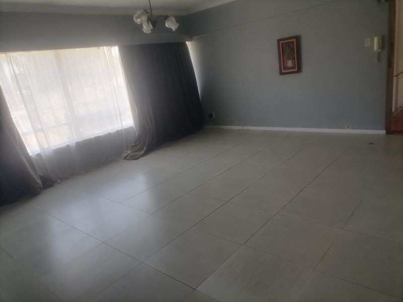 A spacious, empty living room featuring neutral tiled flooring, a large window with curtains, and an integrated intercom system.