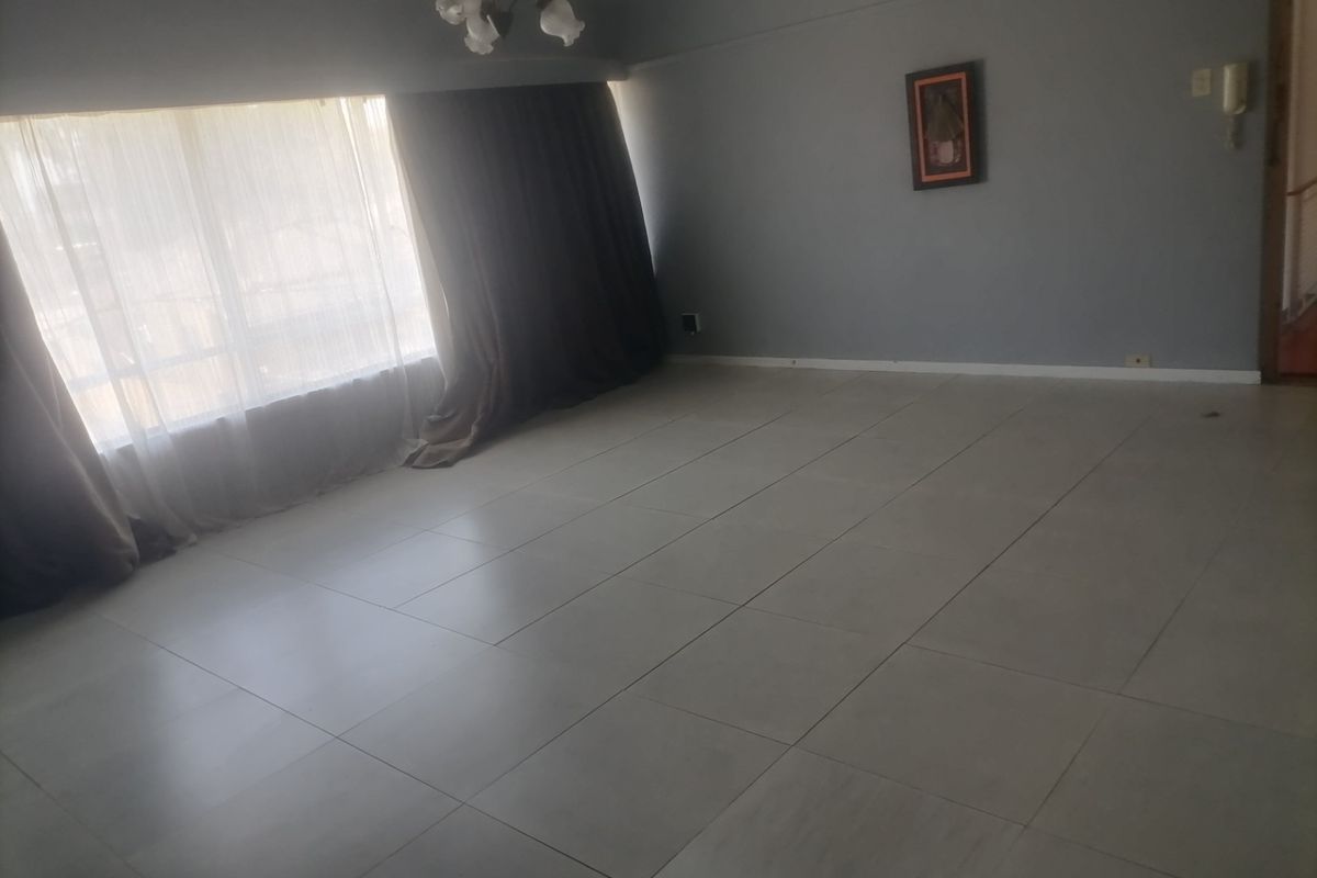 A spacious, empty living room featuring neutral tiled flooring, a large window with curtains, and an integrated intercom system.