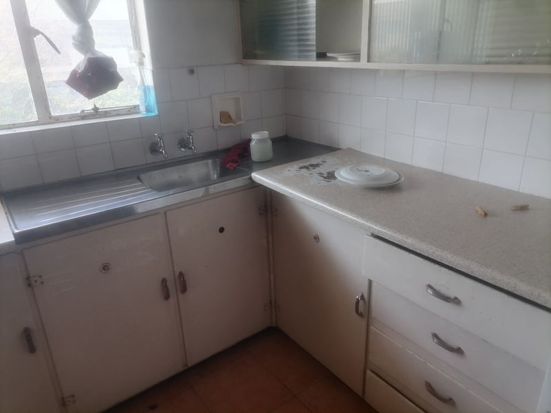 A dated kitchen featuring original cabinetry, laminate countertops, and a stainless steel sink, offering significant potential for a modern renovation.
