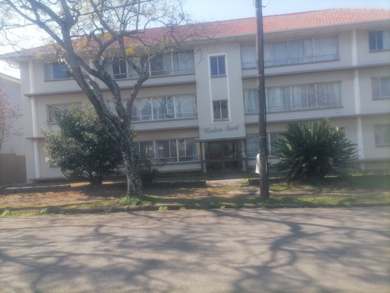 Front elevation of Hinton Court, a multi-story apartment building featuring a tiled roof, large windows, and a central entrance.