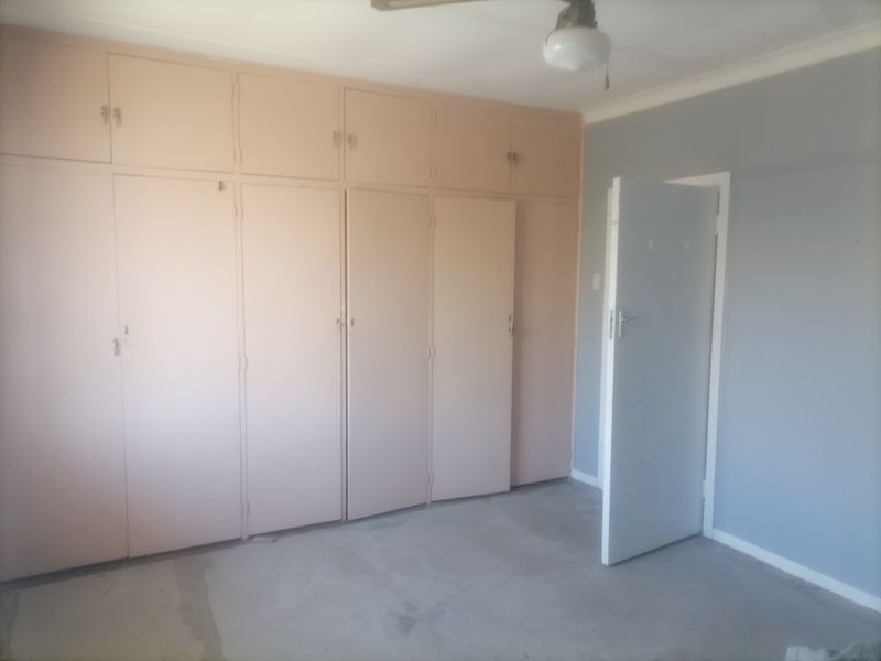 An empty bedroom featuring extensive built-in cupboards and a neutral wall finish, offering a blank canvas for renovation or interior design updates.