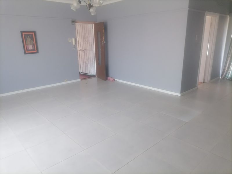 A spacious, empty living area featuring neutral tiled flooring, a security gate at the entrance, and an intercom system.