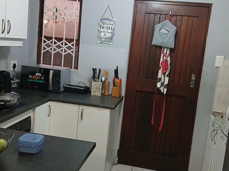 A functional kitchen featuring built-in cabinetry, dark laminate countertops, and a solid timber door with an integrated security gate.