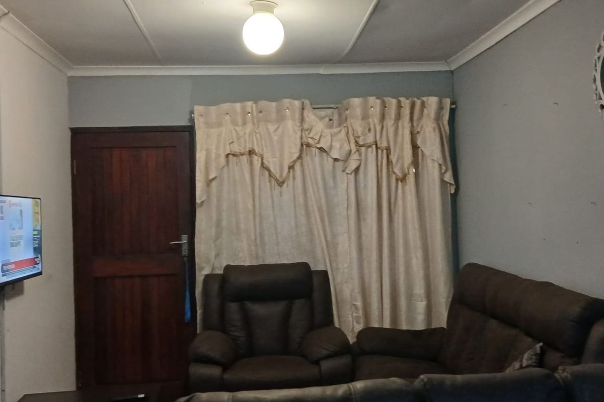 A living room featuring a timber door, ceiling cornice, and basic lighting. The space shows signs of wear and could benefit from cosmetic updates.