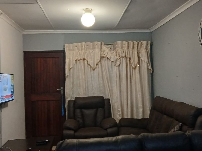 A living room featuring a timber door, ceiling cornice, and basic lighting. The space shows signs of wear and could benefit from cosmetic updates.