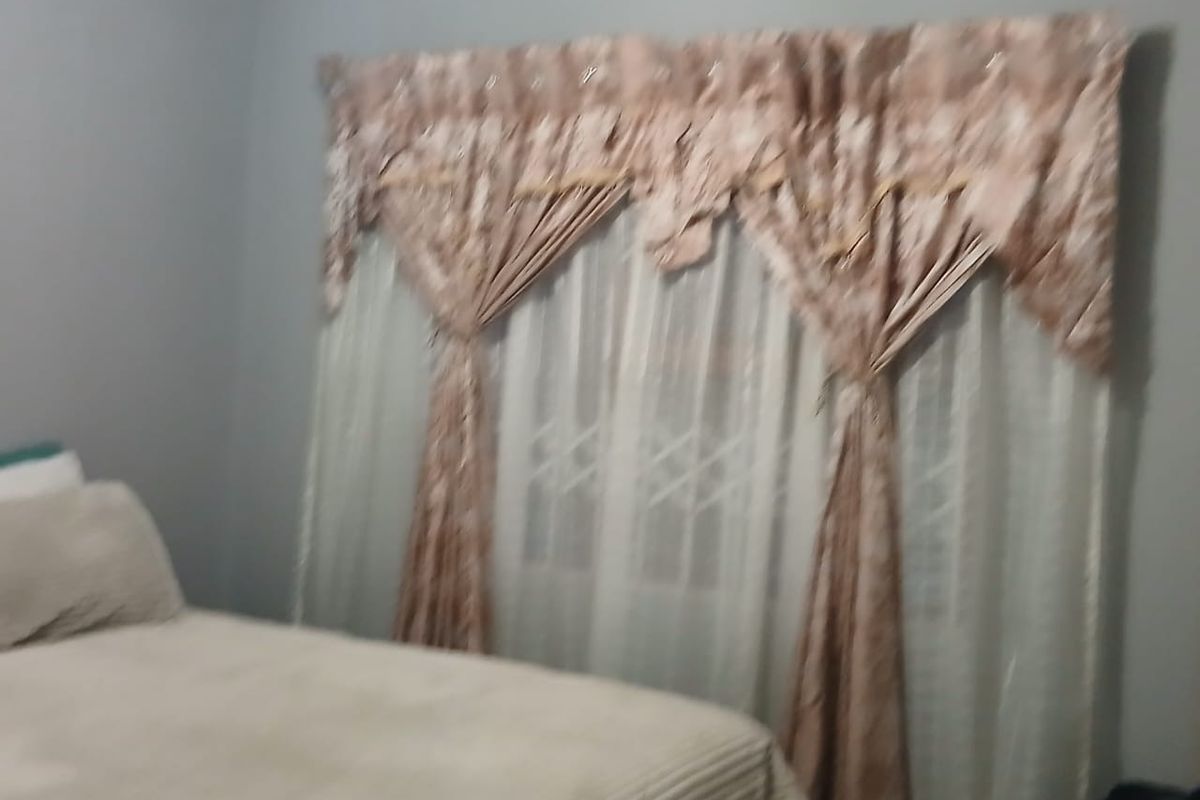 A bedroom featuring a window with security bars and decorative window treatments.