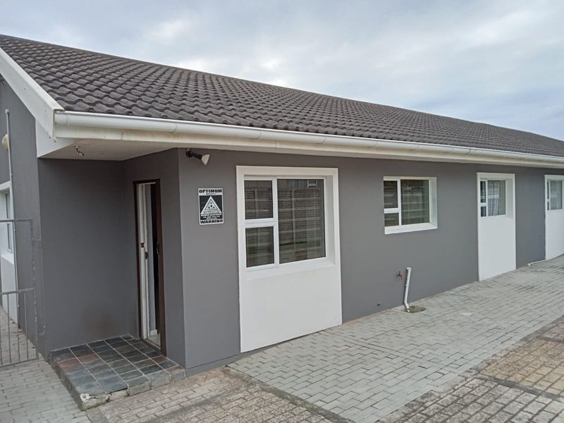 Front elevation of a townhouse featuring a tiled roof, paved driveway, and modern grey exterior finish with white window frames.