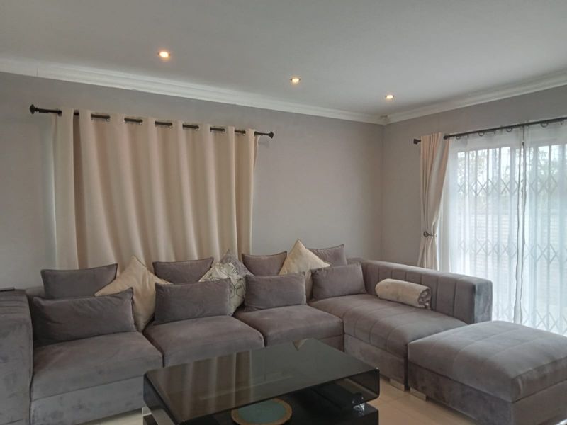 A well-maintained living room featuring recessed downlighting, coved ceilings, and a sliding glass door with an integrated security gate for outdoor access.