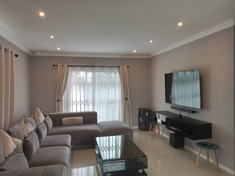 A well-maintained living room featuring tiled flooring, recessed downlighting, and a sliding glass door with a security gate leading to the exterior.