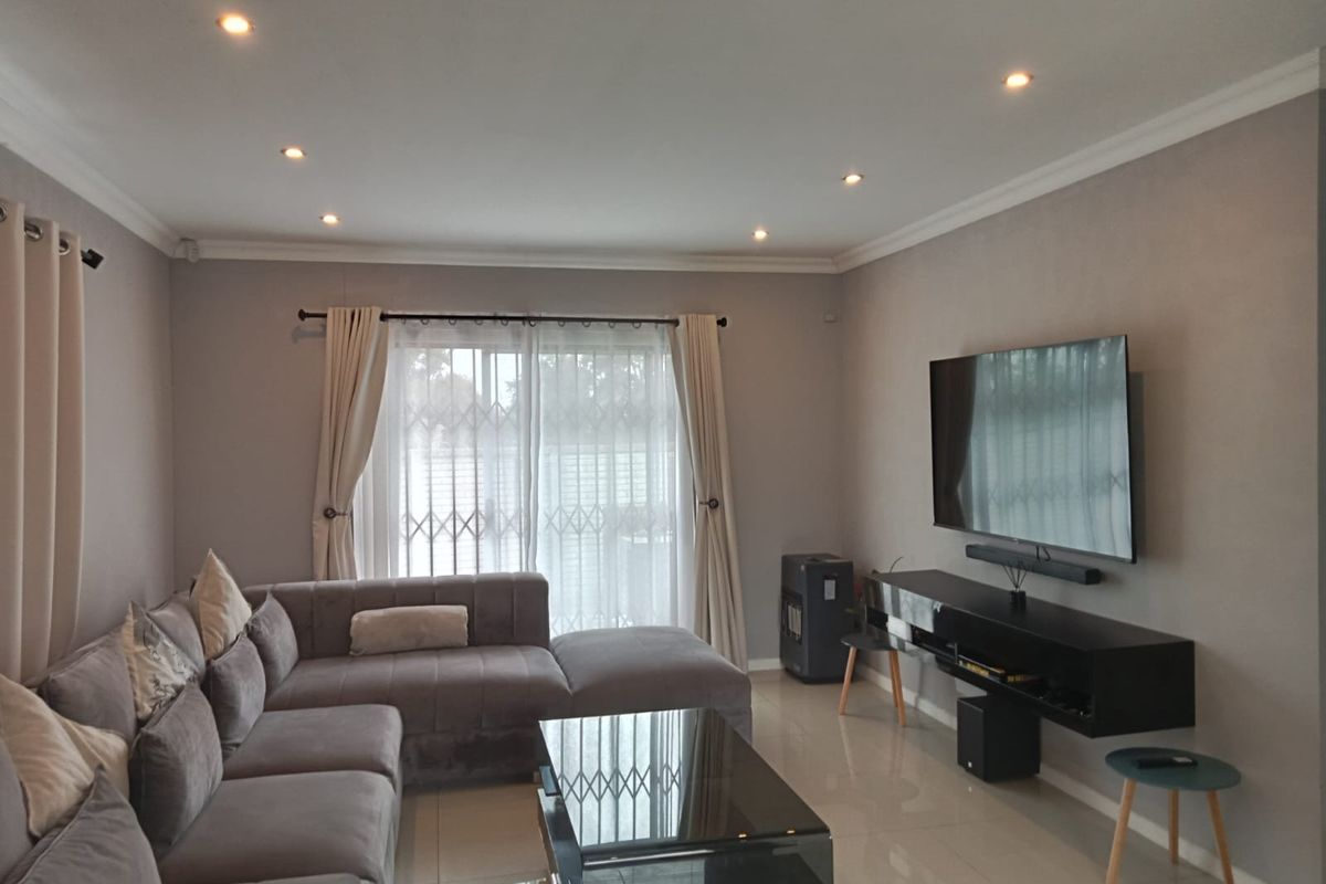 A well-maintained living room featuring tiled flooring, recessed downlighting, and a sliding glass door with a security gate leading to the exterior.