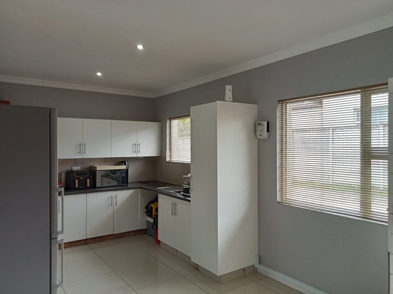 A functional kitchen featuring white cabinetry, dark countertops, tiled flooring, and natural light provided by windows with fitted venetian blinds.