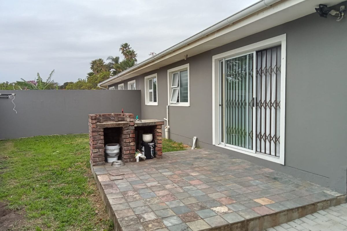 Rear exterior view featuring a paved patio area with a built-in brick braai, sliding door access, and a private garden space.