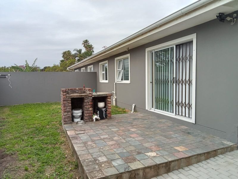 Rear exterior view featuring a paved patio area with a built-in brick braai, sliding door access, and a private garden space.