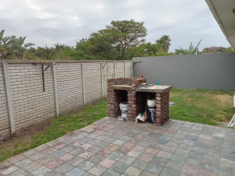 Outdoor patio area featuring a built-in brick braai, slate tile flooring, and enclosed by a combination of brick and concrete boundary walls.
