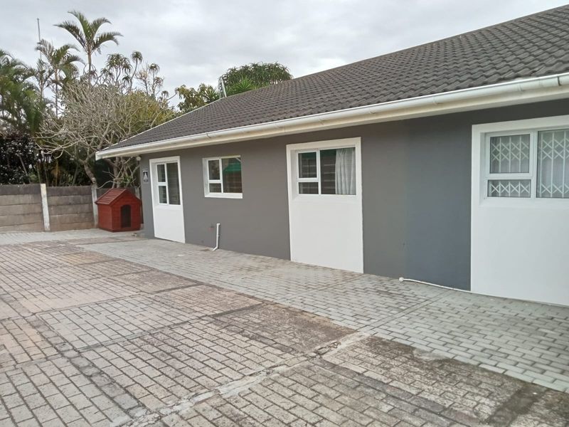 Exterior view of the townhouse featuring a paved driveway, grey painted facade, and secure window fittings under a tiled roof.