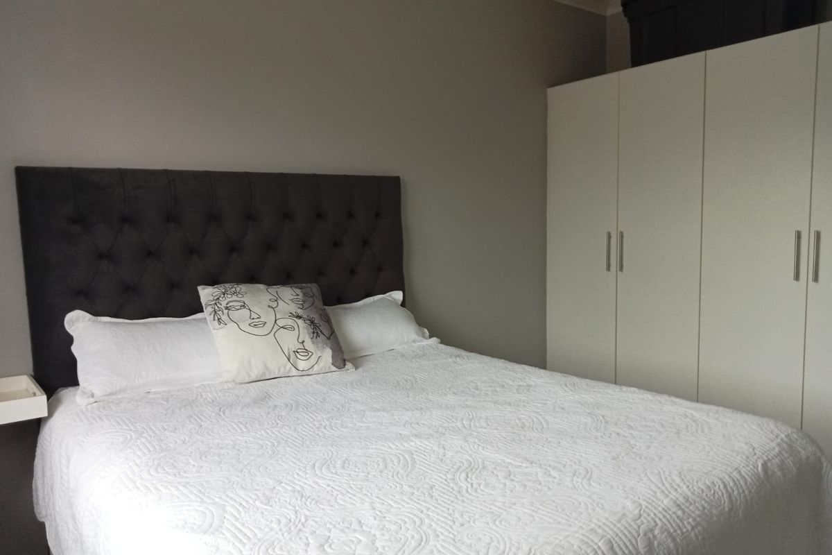 A well-maintained bedroom featuring a neutral color palette, built-in white wardrobe cabinetry, and a floating bedside shelf.