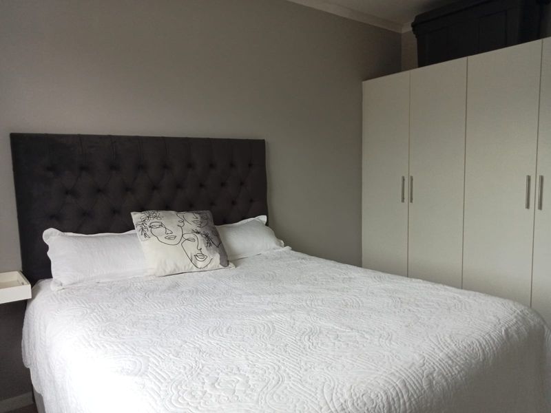 A well-maintained bedroom featuring a neutral color palette, built-in white wardrobe cabinetry, and a floating bedside shelf.