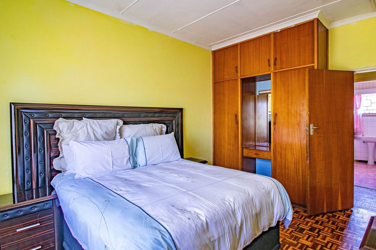 A bedroom featuring built-in wooden cupboards, parquet flooring, and a coved ceiling, with an adjoining bathroom visible through the doorway.