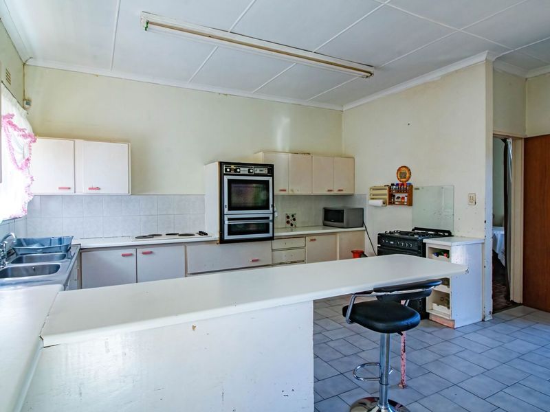 A dated kitchen featuring built-in cabinetry, a double sink, and a breakfast bar, offering significant potential for modernization and renovation.
