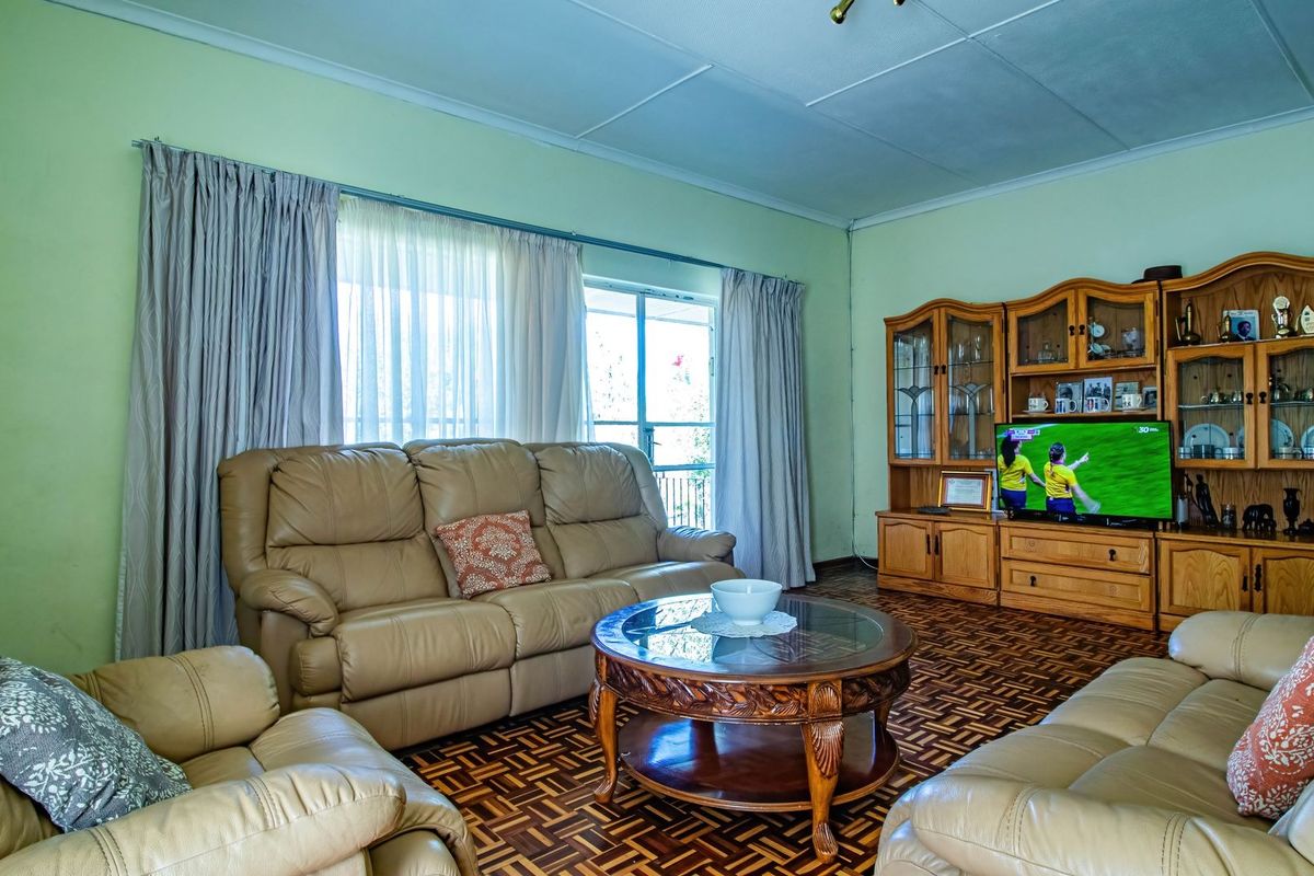 A spacious living room featuring traditional parquet flooring, large sliding glass doors for natural light, and neutral wall finishes.