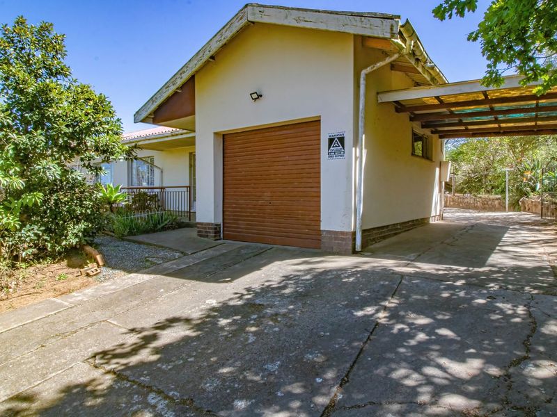 Exterior view of a single garage with an attached carport and a concrete driveway, showing signs of wear and weathering.