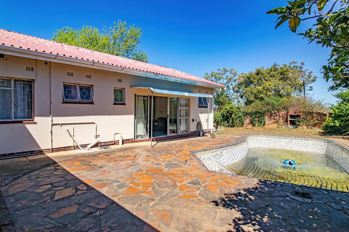 Rear exterior view featuring a stone-paved patio, a swimming pool with safety net, and direct access to the home via sliding glass doors.