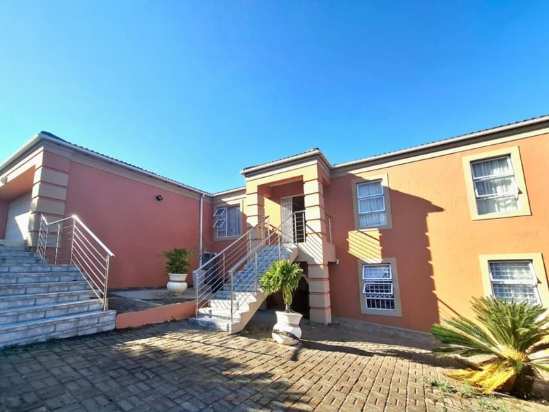 Front exterior view of a multi-level house featuring a paved driveway, tiled staircase with stainless steel balustrades, and plastered facade.