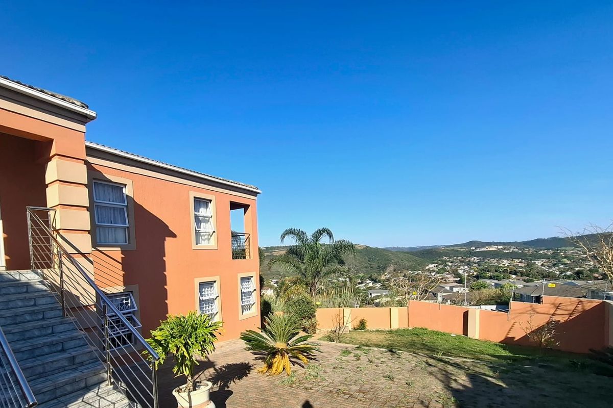 Rear exterior view of the property featuring a paved patio, staircase with stainless steel balustrades, and expansive views of the surrounding landscape.