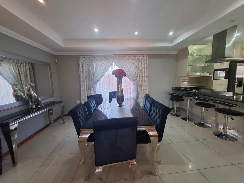 An open-plan dining and kitchen area featuring modern tiled flooring, recessed ceiling lighting, and a sleek breakfast bar with integrated cabinetry and extractor fan.