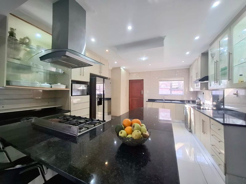 Modern kitchen featuring granite countertops, ample built-in cabinetry, a gas hob with extractor fan, and high-gloss tiled flooring with recessed lighting.
