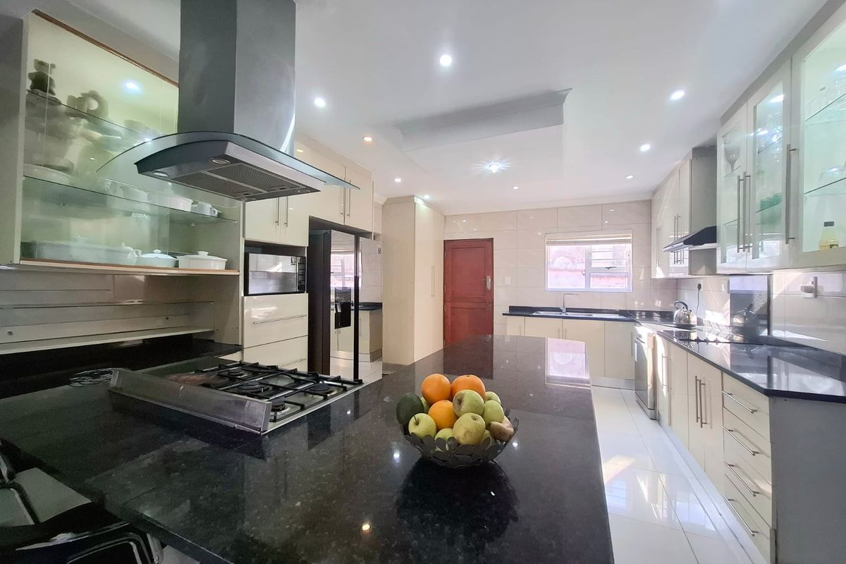 Modern kitchen featuring granite countertops, ample built-in cabinetry, a gas hob with extractor fan, and high-gloss tiled flooring with recessed lighting.