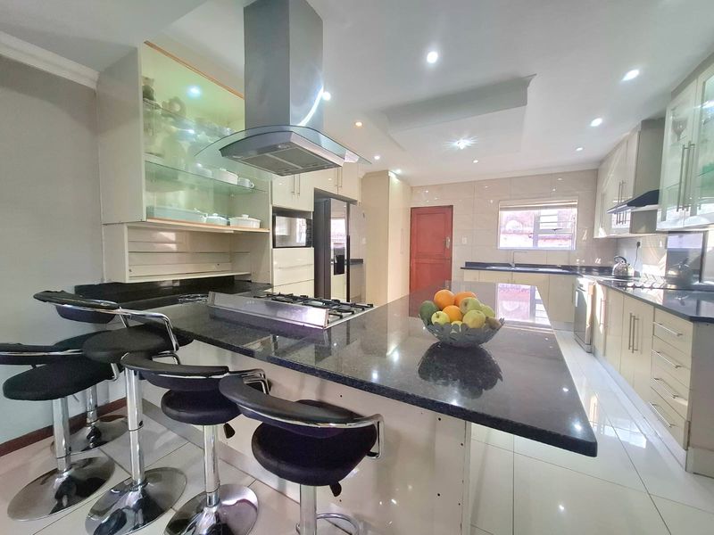 Modern kitchen featuring granite countertops, a central island with a gas hob, stainless steel extractor fan, and ample built-in cabinetry with glass display units.
