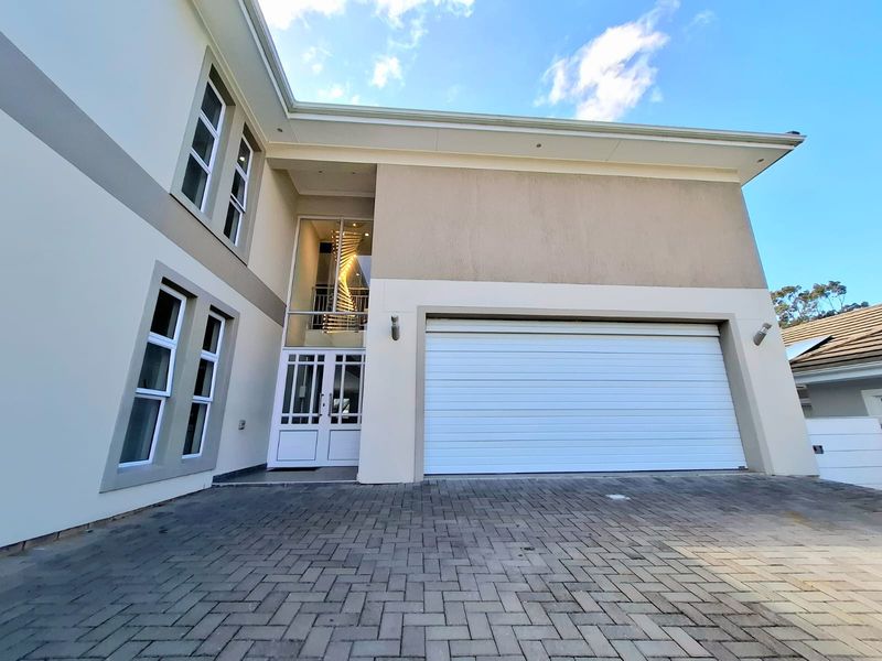 Modern double-story residential facade featuring a paved driveway, double garage, and a striking double-height glass entrance with a visible spiral staircase.