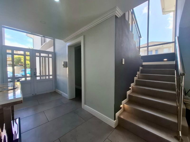 Bright and modern entrance hall featuring tiled flooring, a staircase with stainless steel balustrades, and recessed stair lighting.