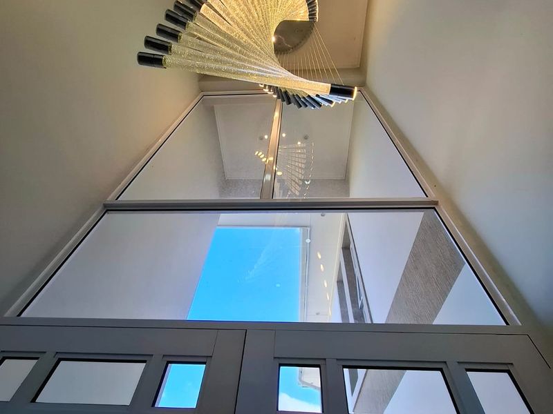 A grand, double-height entrance foyer featuring large glass panels, modern architectural lighting, and a striking contemporary chandelier.