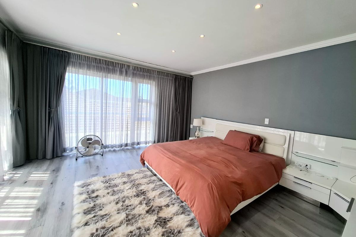Spacious bedroom featuring modern laminate flooring, recessed downlighting, and a built-in headboard with integrated bedside cabinetry, leading to a private outdoor area.