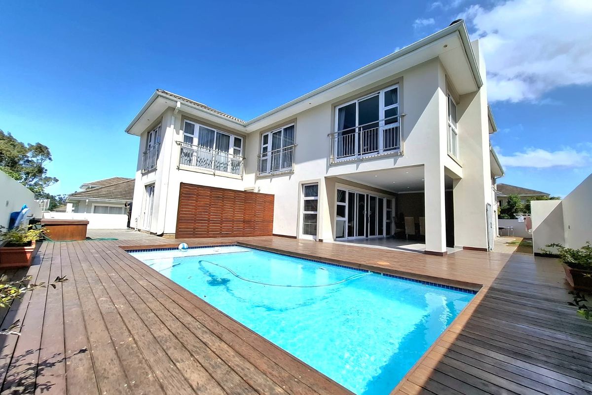 Rear view of the property featuring a swimming pool, timber decking, covered patio area, and upper-level balconies with sliding glass doors.