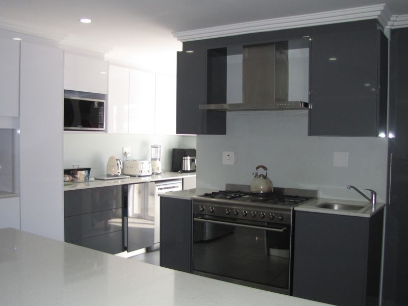 Modern kitchen featuring high-gloss grey and white cabinetry, stone countertops, integrated appliances, and a gas stove with a stainless steel extractor fan.