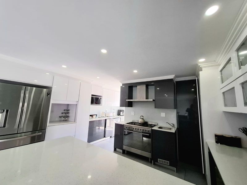 Modern kitchen featuring high-gloss cabinetry, quartz countertops, integrated appliances, and a gas stove with a stainless steel extractor fan.