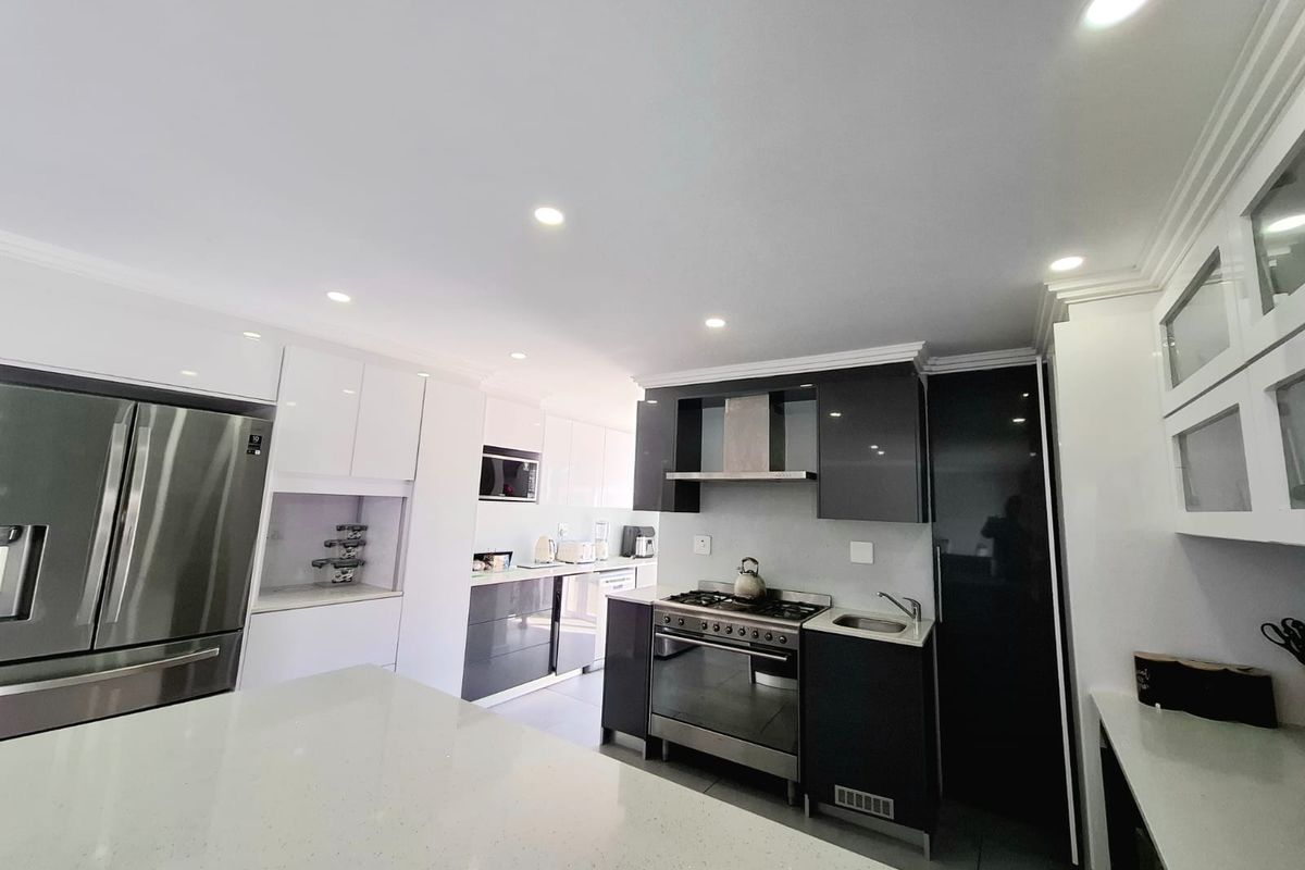 Modern kitchen featuring high-gloss cabinetry, quartz countertops, integrated appliances, and a gas stove with a stainless steel extractor fan.