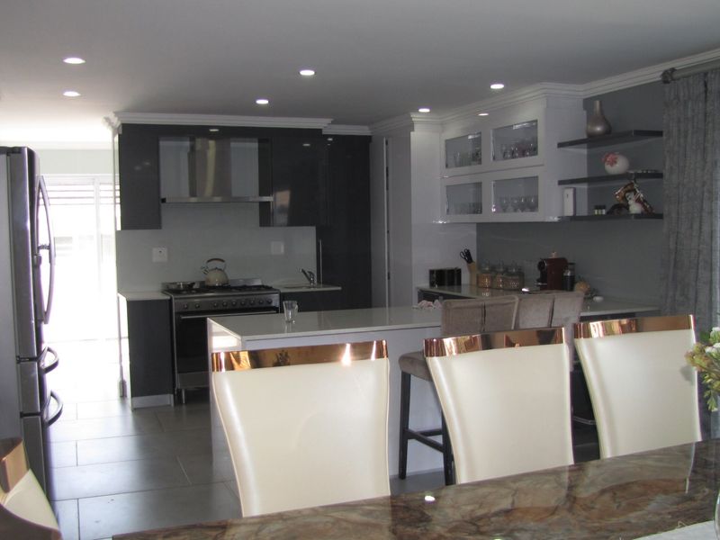 Modern open-plan kitchen featuring a central island, stone countertops, dark cabinetry, and integrated gas stove with extractor fan.